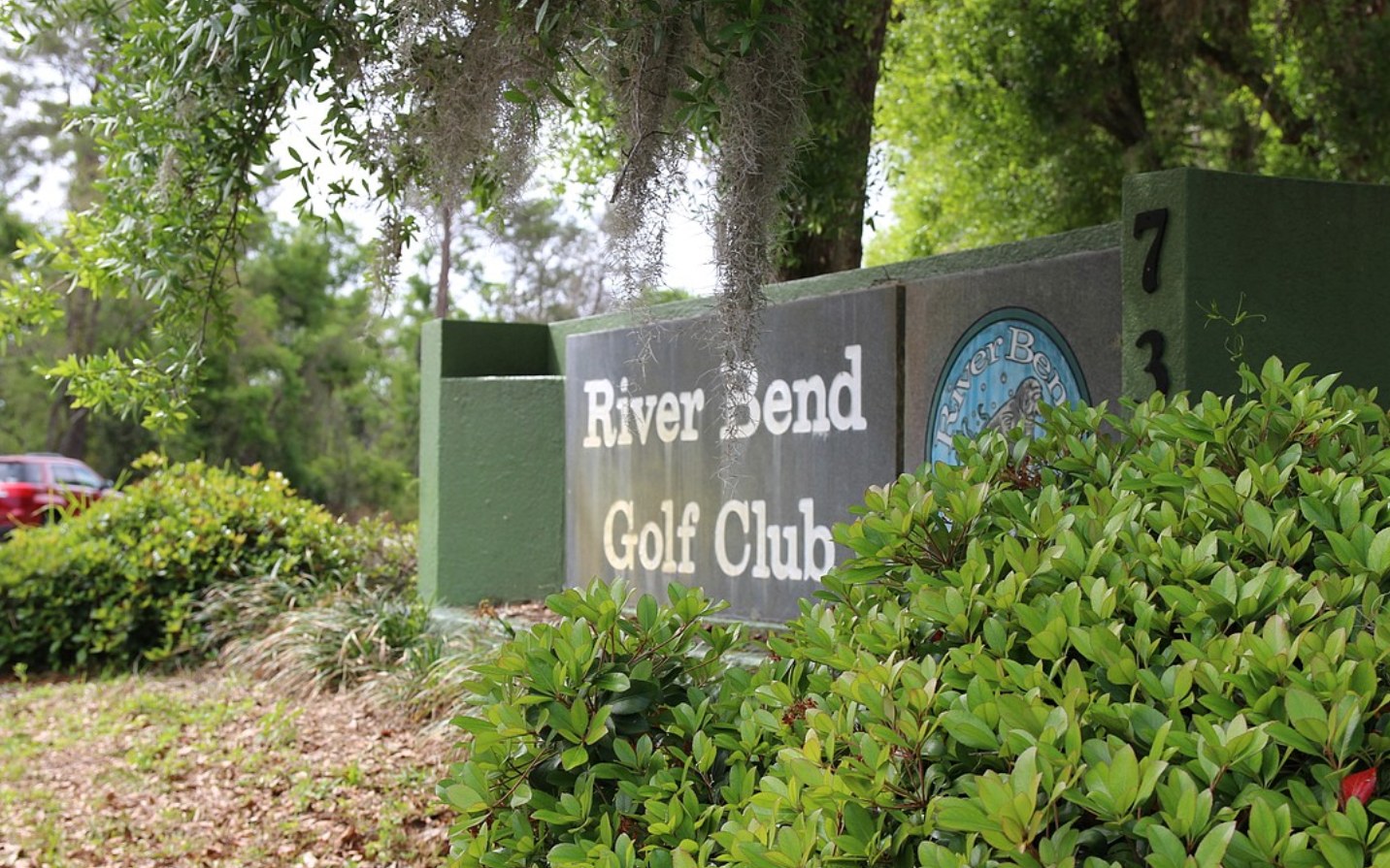 The River Bend Golf Club entrance sign framed by Spanish moss and green shrubs.