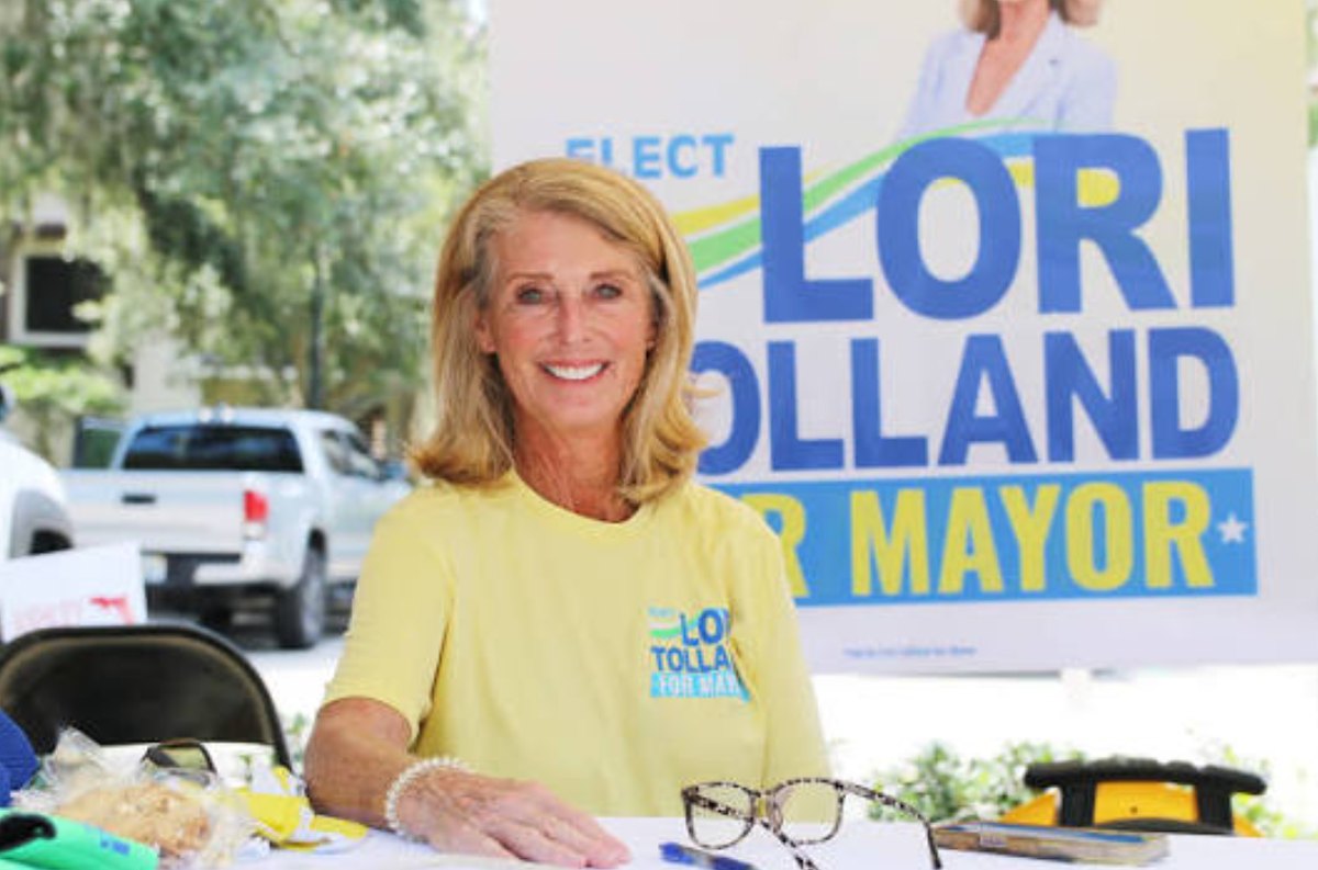 Lori Tolland smiling at a campaign table in front of an 'Elect Lori Tolland for Mayor' banner.