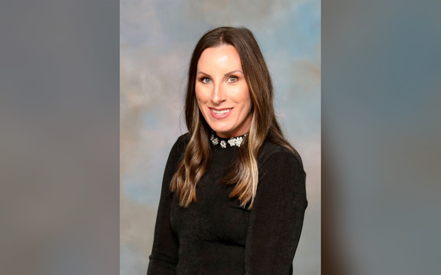 Portrait of Zone 3 City Commissioner Kristin Deaton smiling in a black top against a soft blue studio backdrop.